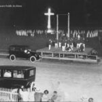 A car driving down the road near a cross.