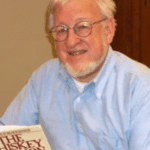A man with glasses and a beard holding a book.