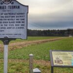 A sign in front of a field with a historical marker.