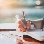 A person writing on paper with pen and notebook.