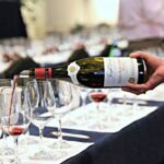 A person pouring wine into glasses on a table.