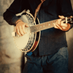 A man playing the banjo in front of a wall.