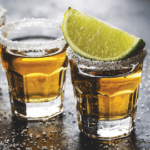 Two shot glasses with tequila and a lime wedge.