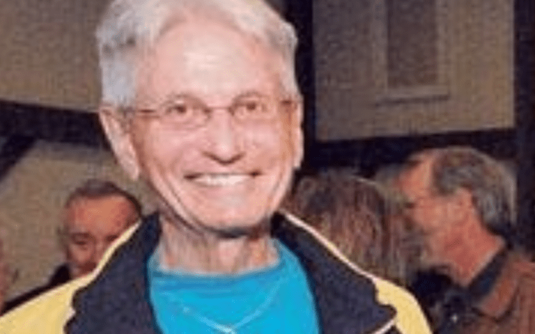 A man with white hair and glasses smiling.