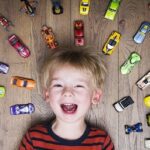 A boy laying on the ground with toy cars around him.