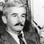 A man with a mustache holding a pipe.