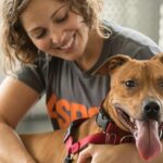 A woman holding onto the chin of a brown dog.