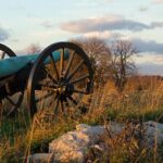 A cannon sitting in the grass near some rocks.