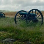 Two old guns sitting in a field with grass