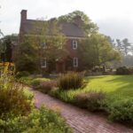 A brick walkway leading to a house with a garden.