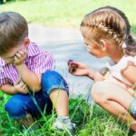 Two children sitting in the grass talking to each other.