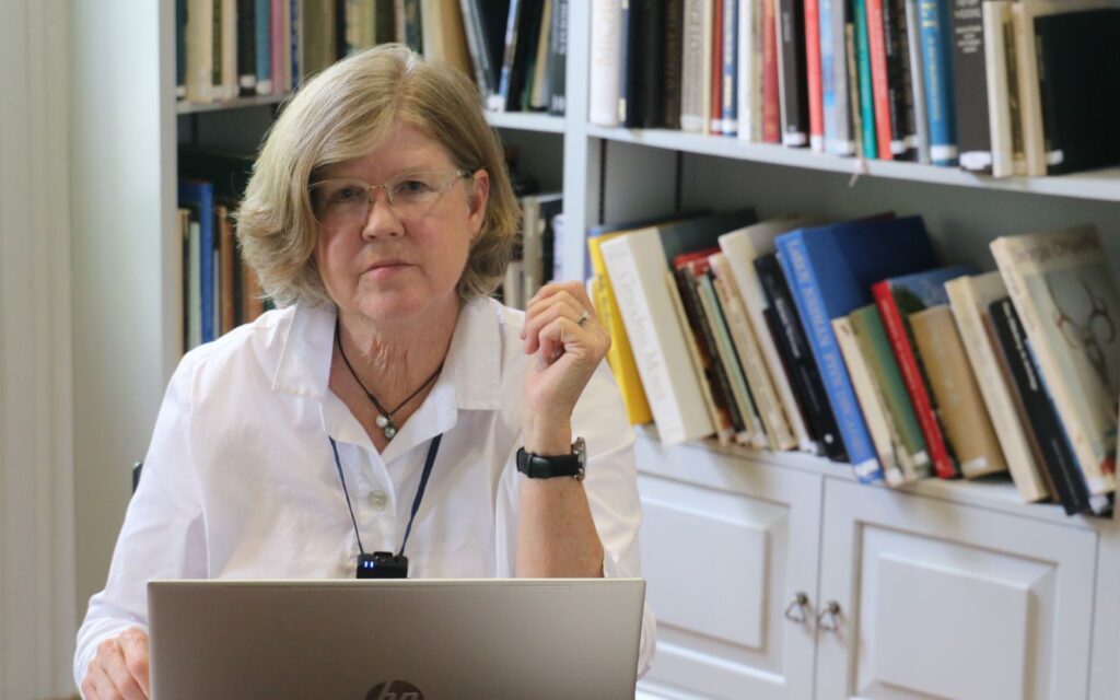 A woman sitting at her laptop in front of some books.