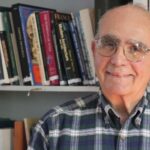 A man in glasses standing next to books.