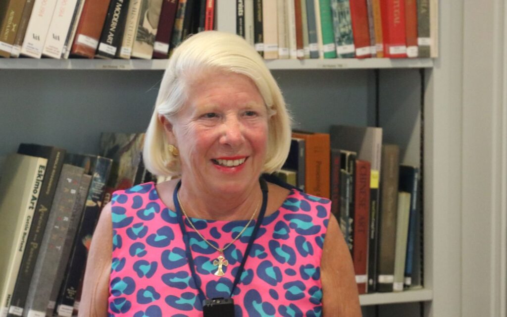A woman in a pink and blue dress standing next to books.