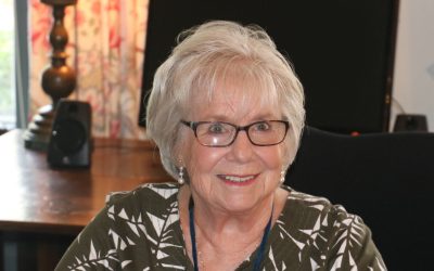 A woman with glasses sitting in front of a curtain.
