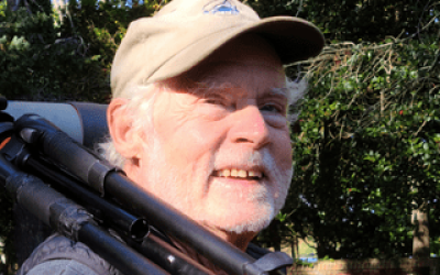 A man with a beard and hat holding a rifle.