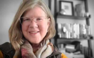 A woman with glasses and scarf smiling for the camera.
