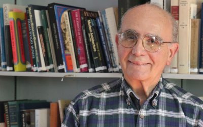 A man in glasses standing next to books.